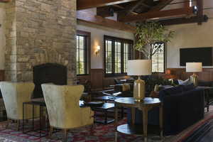 Living room featuring beamed ceiling, a stone fireplace, and a towering ceiling