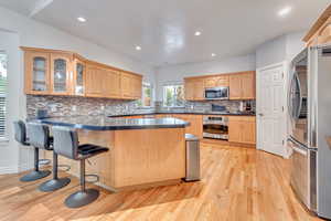 Kitchen with a kitchen breakfast bar, backsplash, appliances with stainless steel finishes, kitchen peninsula, and light wood-type flooring