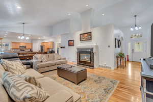 Living room featuring a tiled fireplace, high vaulted ceiling, light hardwood / wood-style flooring, and a notable chandelier