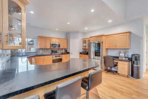 Kitchen featuring built in desk, appliances with stainless steel finishes, light hardwood / wood-style floors, kitchen peninsula, and a kitchen breakfast bar