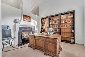 Carpeted office space featuring vaulted ceiling and a tiled fireplace