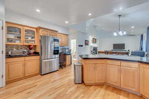 Kitchen featuring an inviting chandelier, stainless steel fridge, pendant lighting, light hardwood / wood-style flooring, and decorative backsplash