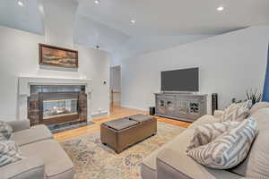 Living room with lofted ceiling, a tiled fireplace, and hardwood / wood-style flooring