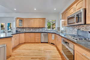 Kitchen featuring light brown cabinetry, light wood-type flooring, appliances with stainless steel finishes, and tasteful backsplash