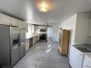 Kitchen featuring appliances with stainless steel finishes, a textured ceiling, ceiling fan, sink, and washing machine and clothes dryer