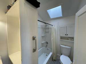 Bathroom featuring shower / bath combo, lofted ceiling with skylight, and toilet