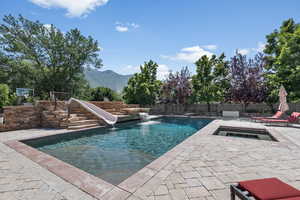 View of pool with pool water feature, a water slide, a patio area, and a mountain view