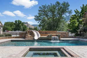 View of swimming pool with a water slide, a patio area, a mountain view, and an in ground hot tub