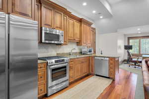 Kitchen featuring light stone counters, sink, decorative backsplash, appliances with stainless steel finishes, and light hardwood / wood-style floors