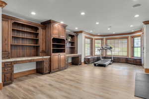 Interior space with light wood-type flooring, built in desk, and ornamental molding