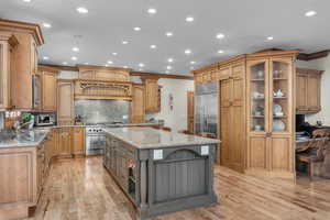 Kitchen featuring built in appliances, light hardwood / wood-style flooring, light stone counters, and a center island