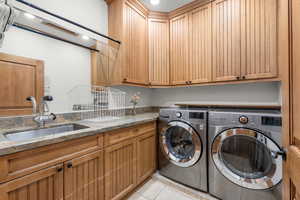 Laundry room with light tile patterned flooring, cabinets, washer and clothes dryer, and sink