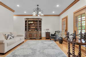 Living area with light wood-type flooring, an inviting chandelier, and crown molding