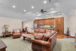 Carpeted living room with ceiling fan, sink, and vaulted ceiling