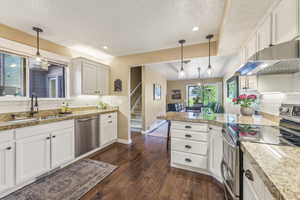 Kitchen with white cabinets, pendant lighting, stainless steel appliances, and sink