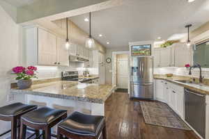 Kitchen with dark hardwood / wood-style floors, a kitchen breakfast bar, appliances with stainless steel finishes, sink, and white cabinets