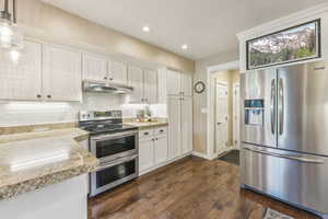 Kitchen with light stone countertops, pendant lighting, dark wood-type flooring, stainless steel appliances, and white cabinetry