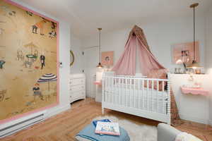 Bedroom featuring a baseboard heating unit, a nursery area, and hardwood / wood-style floors