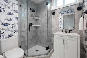 Bathroom with tile walls, toilet, a shower with door, and vanity