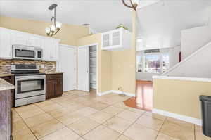 Kitchen with light tile patterned floors, stainless steel appliances, an inviting chandelier, hanging light fixtures, and white cabinets