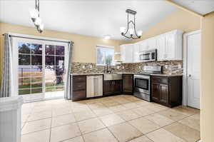 Kitchen with white cabinets, backsplash, decorative light fixtures, stainless steel appliances, and a notable chandelier