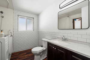 Bathroom featuring vanity, backsplash, wood-type flooring, tile walls, and toilet