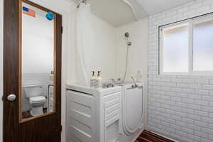 Bathroom with curtained shower, tile walls, wood-type flooring, and toilet