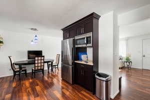 Kitchen featuring dark wood-type flooring, appliances with stainless steel finishes, decorative light fixtures, and dark brown cabinets