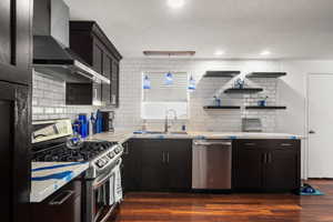 Kitchen featuring dark hardwood / wood-style flooring, sink, decorative backsplash, wall chimney exhaust hood, and appliances with stainless steel finishes