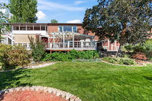 Rear view of house with a wooden deck, a lawn, and a sunroom