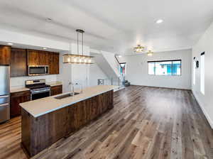 Kitchen with hardwood / wood-style floors, decorative light fixtures, sink, light stone countertops, and appliances with stainless steel finishes