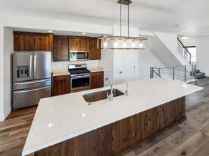 Kitchen with light stone countertops, wood-type flooring, hanging light fixtures, stainless steel appliances, and sink