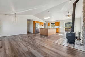 Kitchen with stainless steel fridge, a wood stove, a kitchen island, light wood-type flooring, and vaulted ceiling