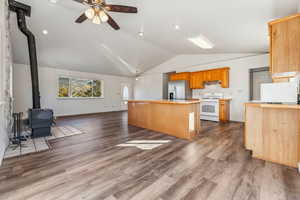 Kitchen with a kitchen island, a wood stove, vaulted ceiling, stainless steel fridge with ice dispenser, and white range