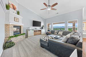 Carpeted living room featuring crown molding, ceiling fan, high vaulted ceiling, and a fireplace