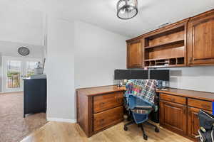 Home office featuring built in desk, a textured ceiling, and light hardwood / wood-style flooring