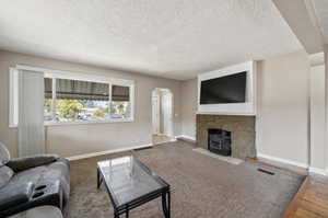 Living room with hardwood / wood-style floors, a textured ceiling, and a stone fireplace