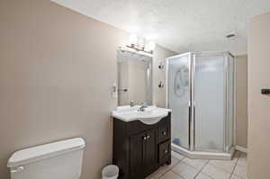 Bathroom featuring a textured ceiling, vanity, an enclosed shower, toilet, and tile patterned floors