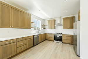 Kitchen featuring light hardwood / wood-style flooring, backsplash, stainless steel appliances, sink, and wall chimney range hood. 2411 S.