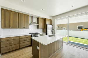 Kitchen features light wood-type flooring, a wealth of natural light, an island with a sink, and a wall chimney range hood. 2425 S.