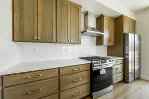 Kitchen featuring light wood-type flooring, appliances with stainless steel finishes, decorative backsplash, and wall chimney exhaust hood. 2425 S.