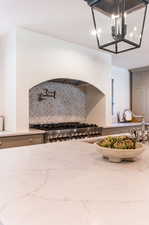 Interior space with tasteful backsplash, gray cabinetry, stainless steel range, an inviting chandelier, and light stone countertops