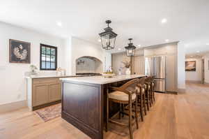 Kitchen with an island with sink, light hardwood / wood-style floors, built in fridge, and hanging light fixtures