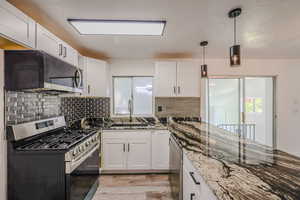 Kitchen featuring light hardwood / wood-style flooring, stone countertops, appliances with stainless steel finishes, sink, and white cabinetry