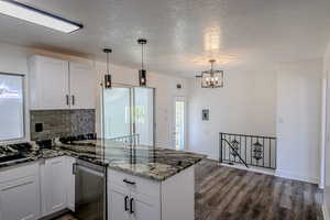 Kitchen featuring an inviting chandelier, wood-type flooring, white cabinets, and decorative backsplash