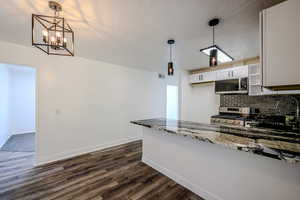 Kitchen featuring decorative light fixtures, stainless steel appliances, dark stone counters, and white cabinetry