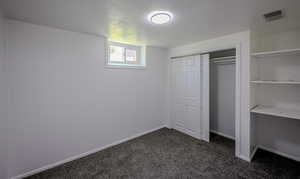 Unfurnished bedroom with a textured ceiling, dark colored carpet, and a closet