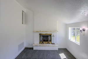 Unfurnished living room featuring vaulted ceiling, dark colored carpet, a textured ceiling, and a brick fireplace