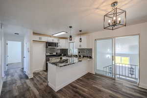 Kitchen with hanging light fixtures, appliances with stainless steel finishes, dark stone counters, dark wood-type flooring, and decorative backsplash