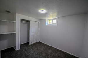 Unfurnished bedroom with a textured ceiling, dark colored carpet, and a closet